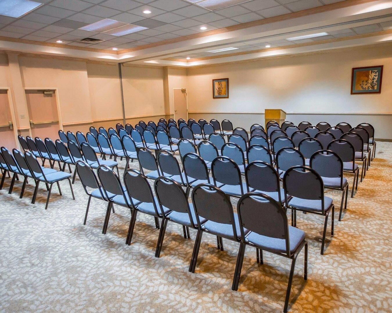 A conference room with rows of chairs, a carpeted floor, and a ceiling with recessed lighting.