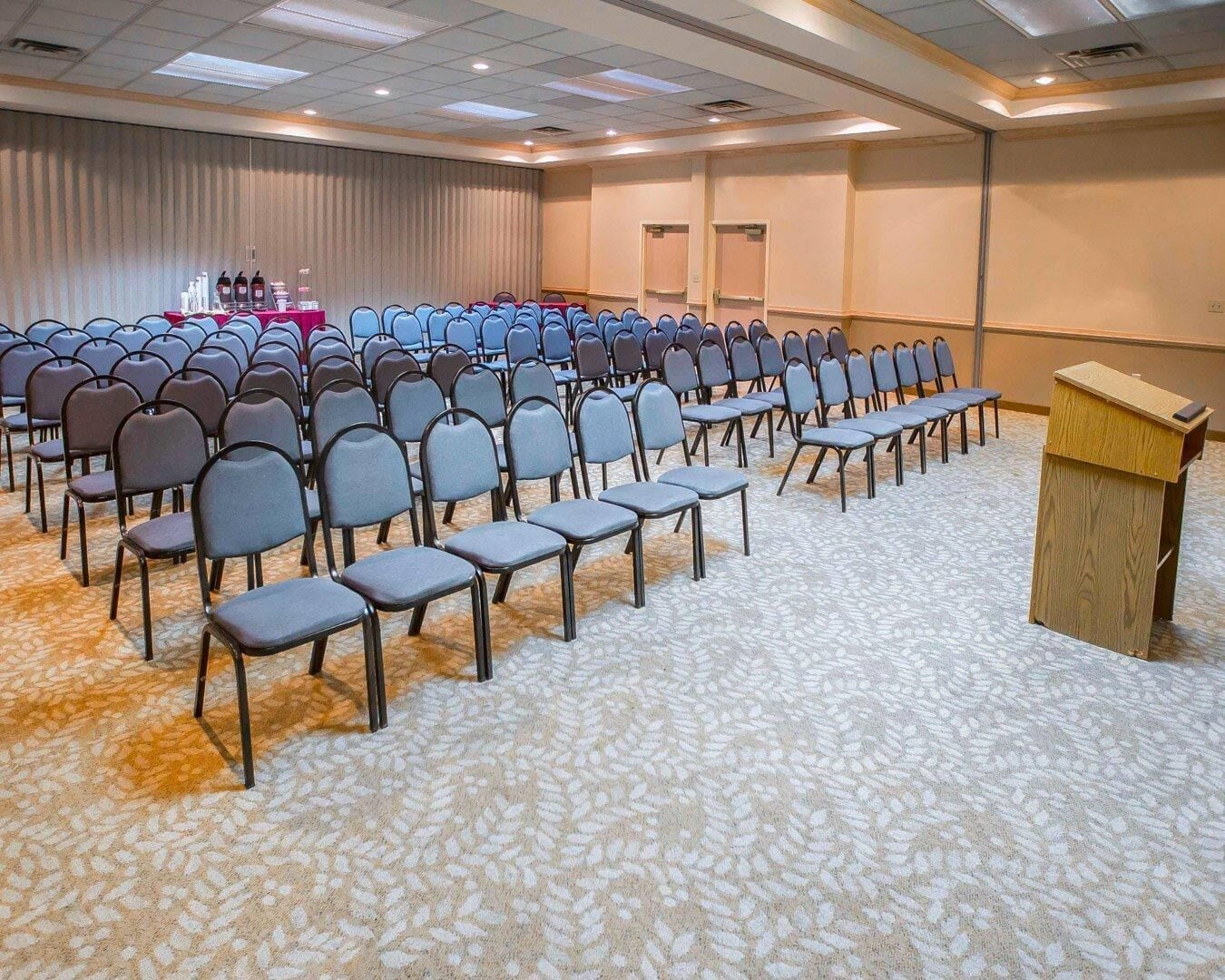 A conference room with rows of chairs, a podium, and a carpeted floor.