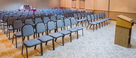 Un salón de conferencias con filas de sillas, un atril y suelo alfombrado.