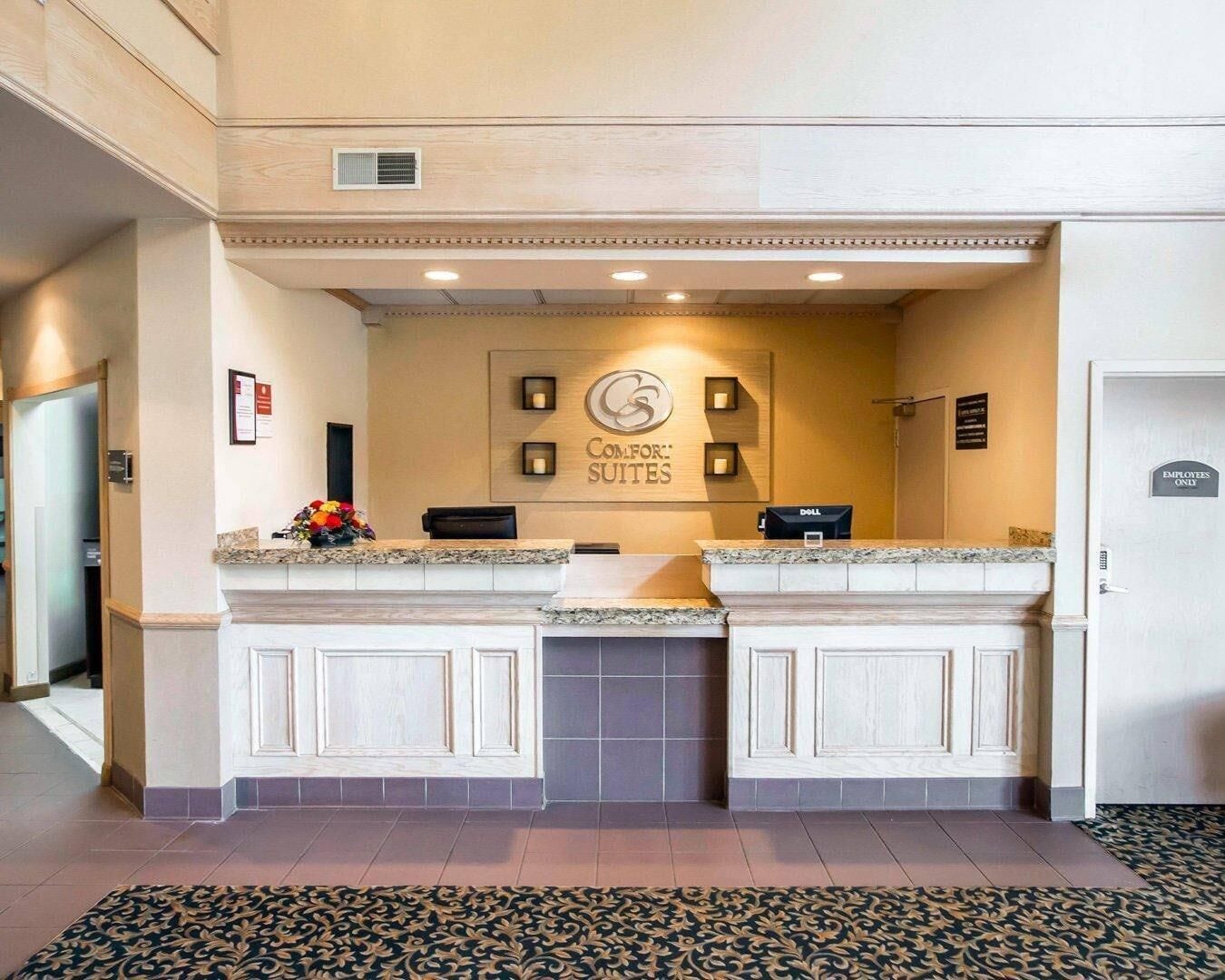 A hotel reception area with a sign for 'Comfort Suites,' a reception desk, a Dell computer, and a 'Employees Only' door.