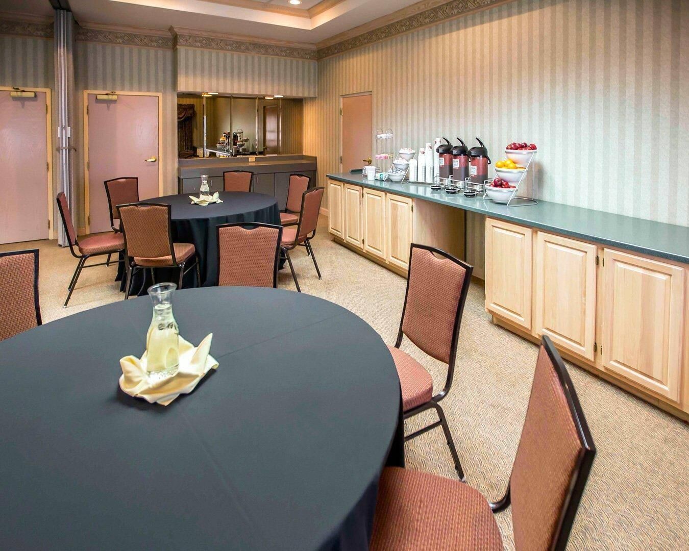Uma sala de conferências com uma mesa redonda, cadeiras, um buffet com comida e bebidas, e um espelho na parede.