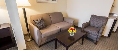 A hotel room with a sofa, armchair, coffee table, and a lamp.