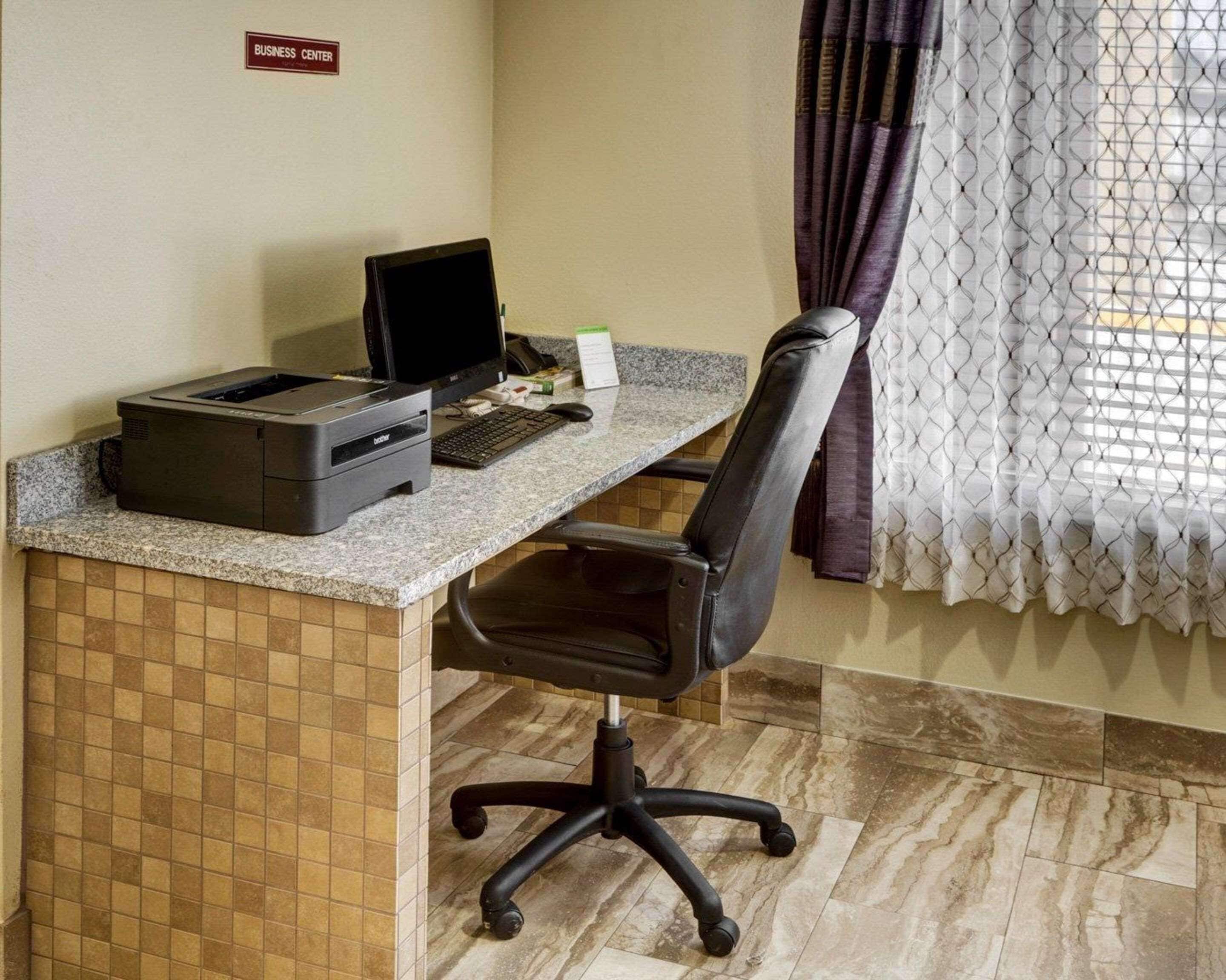 A business center desk with a printer, computer, and keyboard.