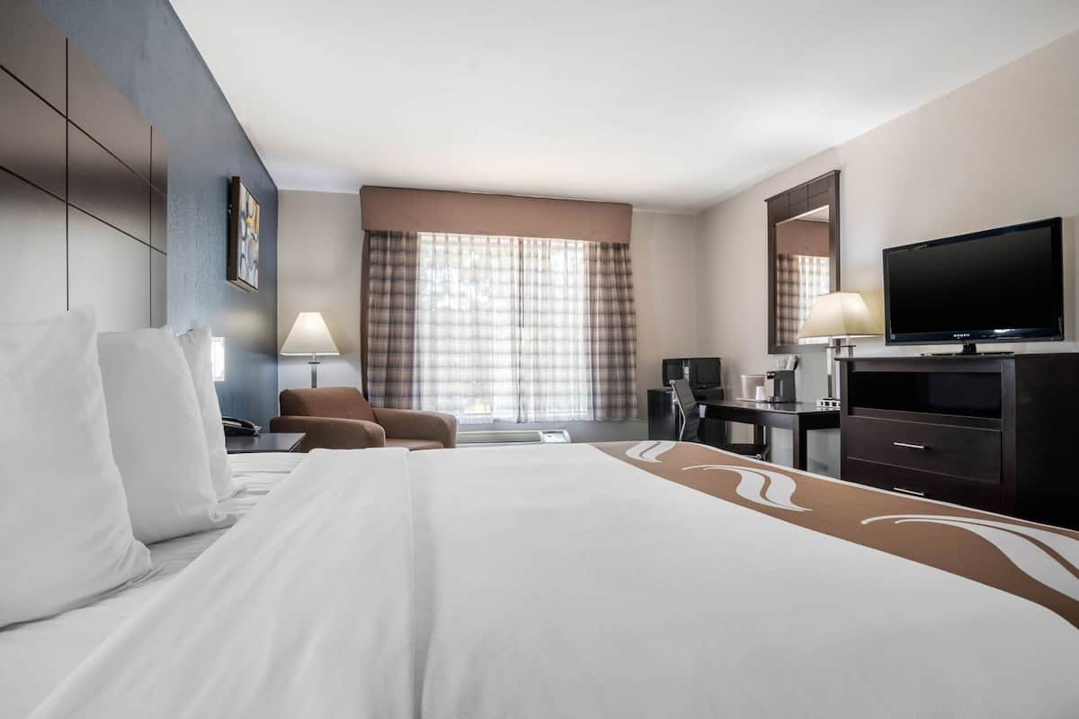 Ett hotellrum med en säng, ett skrivbord, en stol, en tv och ett fönster med gardiner.