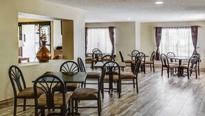 A dining area with multiple tables and chairs, a vase on a counter, and large windows with curtains. - Quality Suites Baton Rouge East - Denham Springs (Baton Rouge)