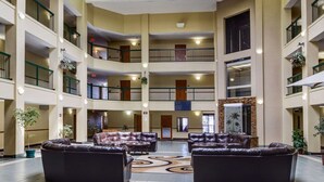 A multi-level hotel lobby with leather sofas, a central decorative rug, and multiple balconies with plants. - Quality Suites Baton Rouge East - Denham Springs (Baton Rouge)