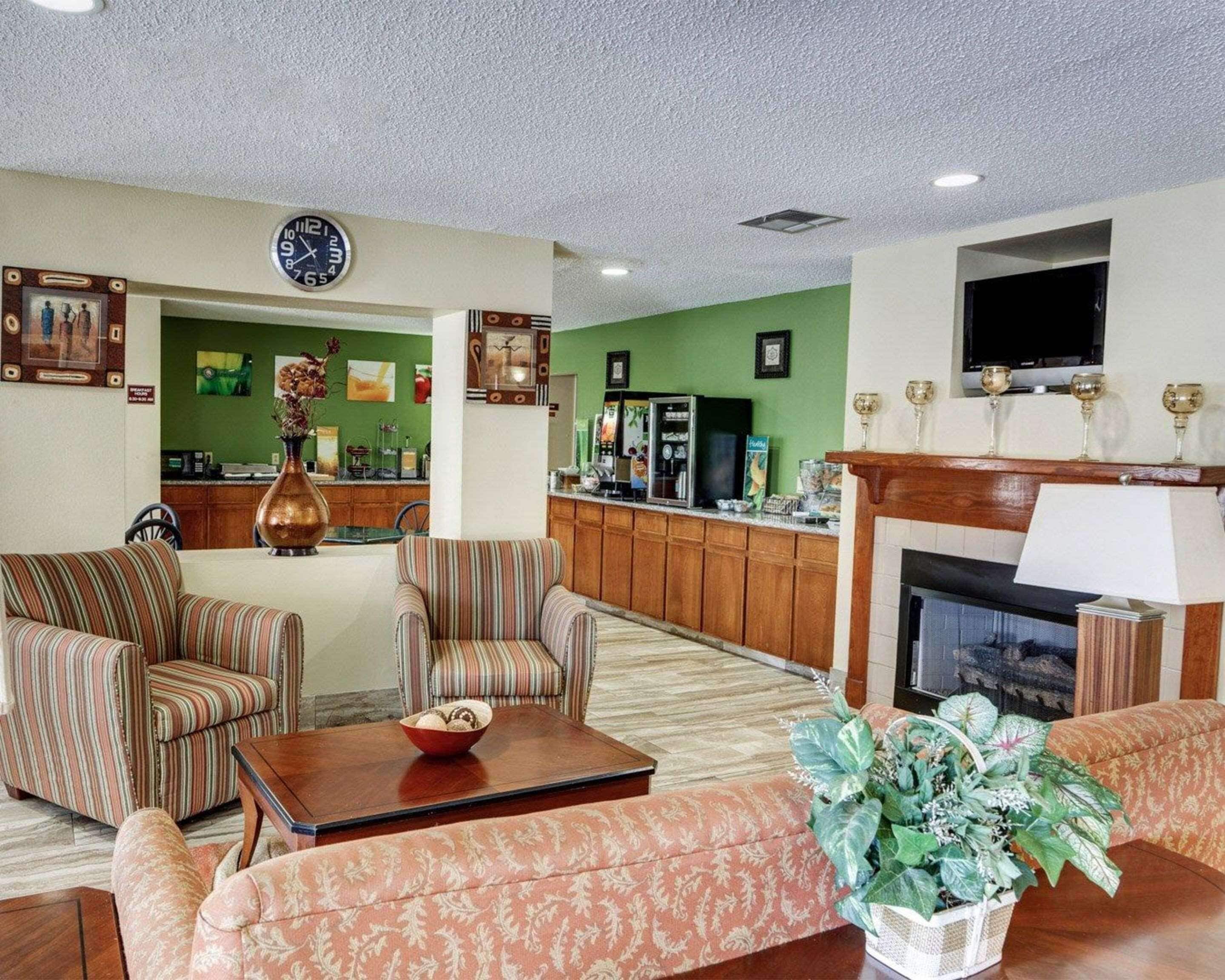 Un vestíbulo de hotel con sofás a rayas, una mesa de centro, una chimenea, un televisor y una zona de cocina al fondo.