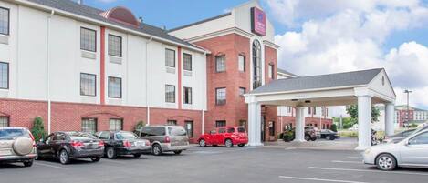 A hotel with a parking lot, a covered entrance, and a brick building with a sign for Courtyard Suites.