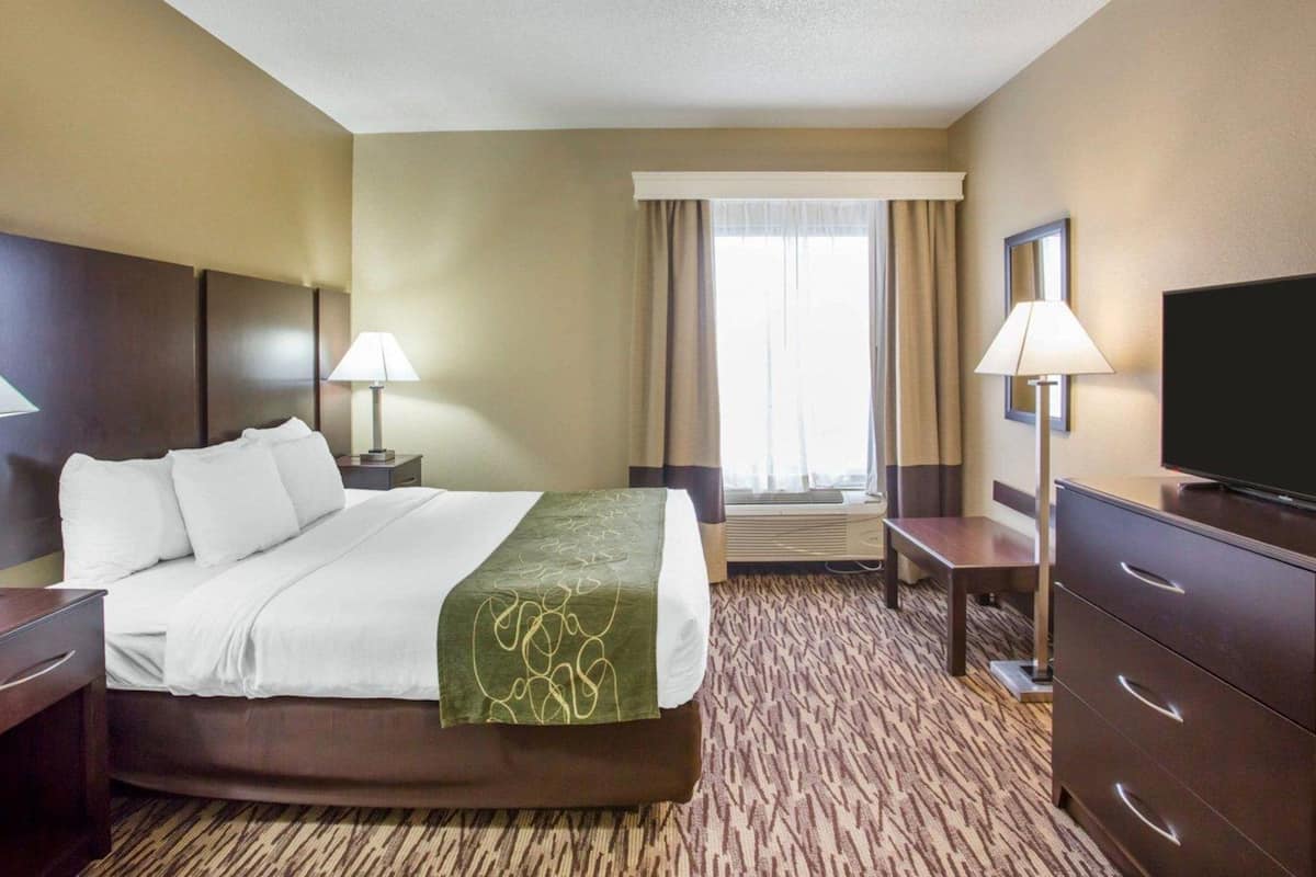 A hotel room with a bed, two bedside tables, a television, a dresser, and a window with curtains.