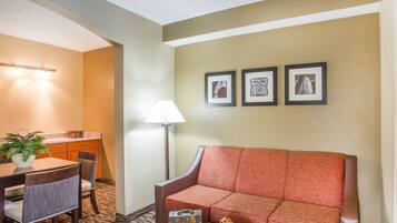Una habitación de hotel con sofá, una mesa de comedor con sillas, una lámpara y tres cuadros en la pared.