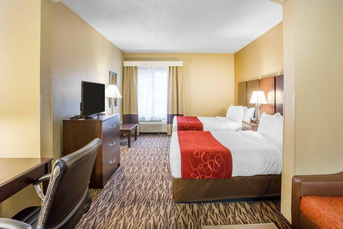A hotel room with a bed, a desk with a TV, a chair, and a window with curtains.