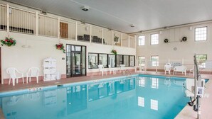 Una piscina interior con agua cristalina, rodeada de sillas blancas y una cubierta superior con ventanas.