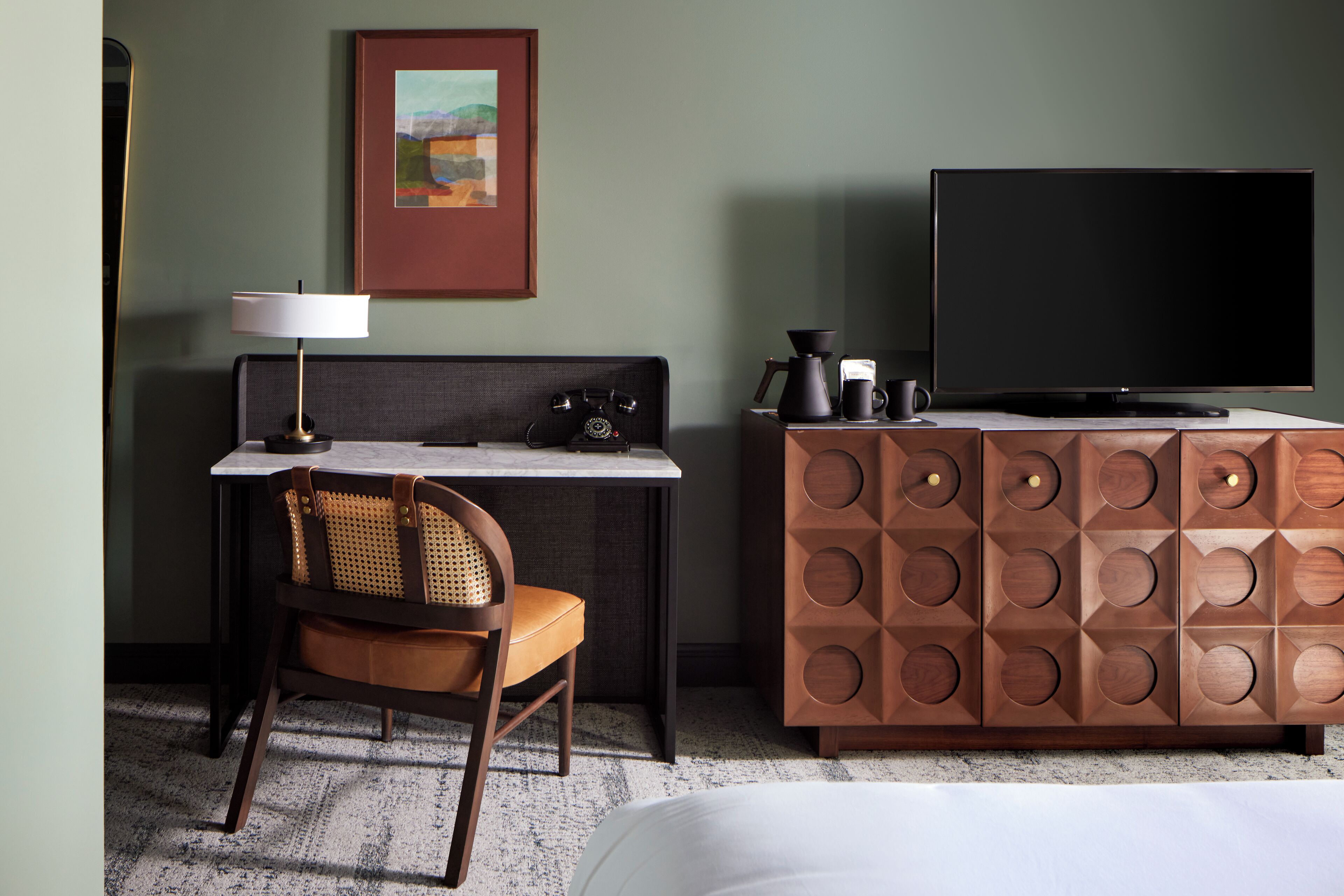 Ein Hotelzimmer mit Bett, Schreibtisch mit Lampe, Fernseher, Kaffeemaschine und Schrank.