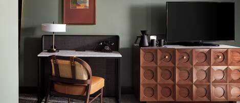 Ein Hotelzimmer mit Bett, Schreibtisch mit Lampe, Fernseher, Kaffeemaschine und Schrank.