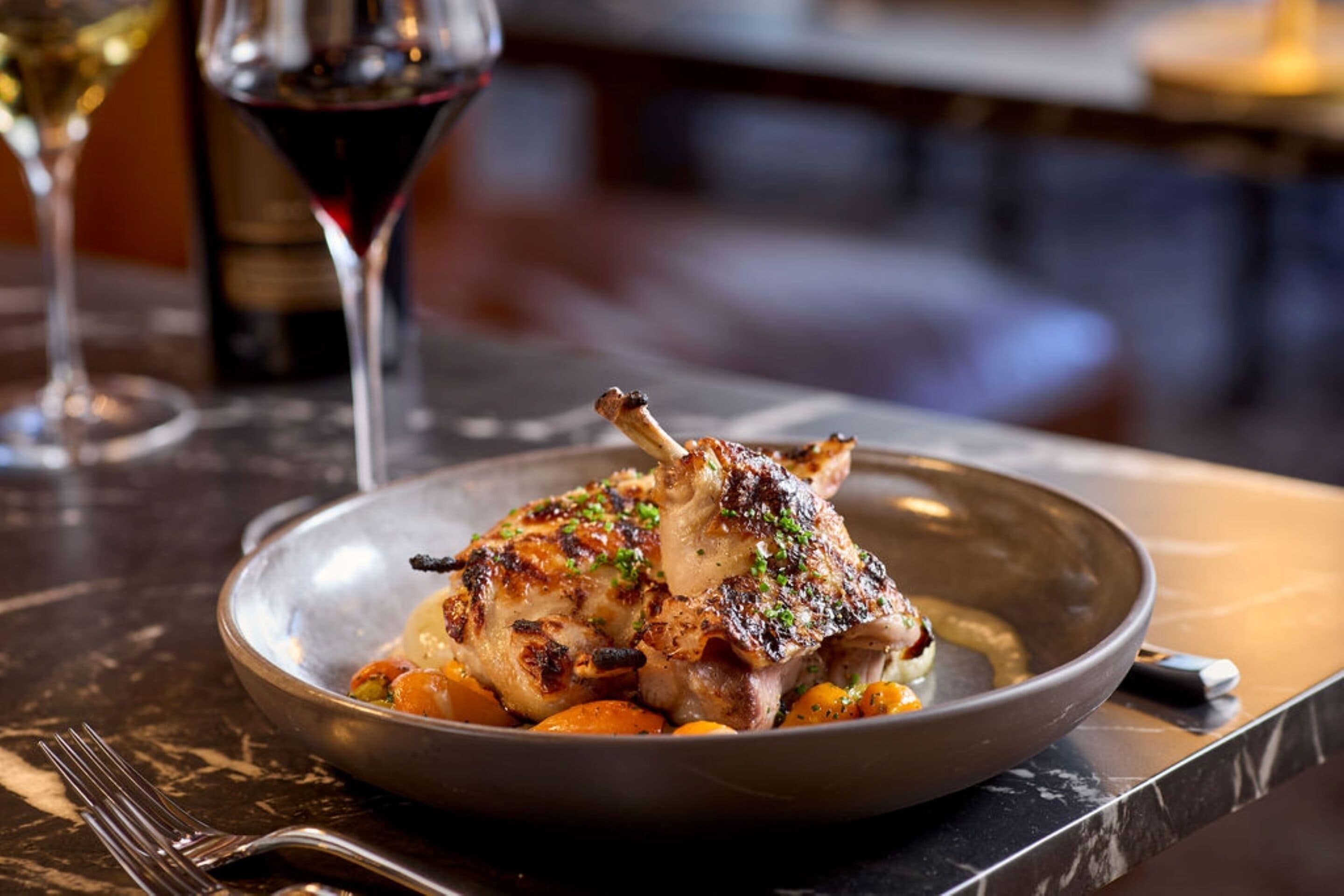 A plate of roasted chicken with vegetables on a dark marble table.