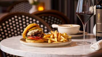 Una mesa con una hamburguesa, papas fritas, una copa de vino tinto y una botella de vino.