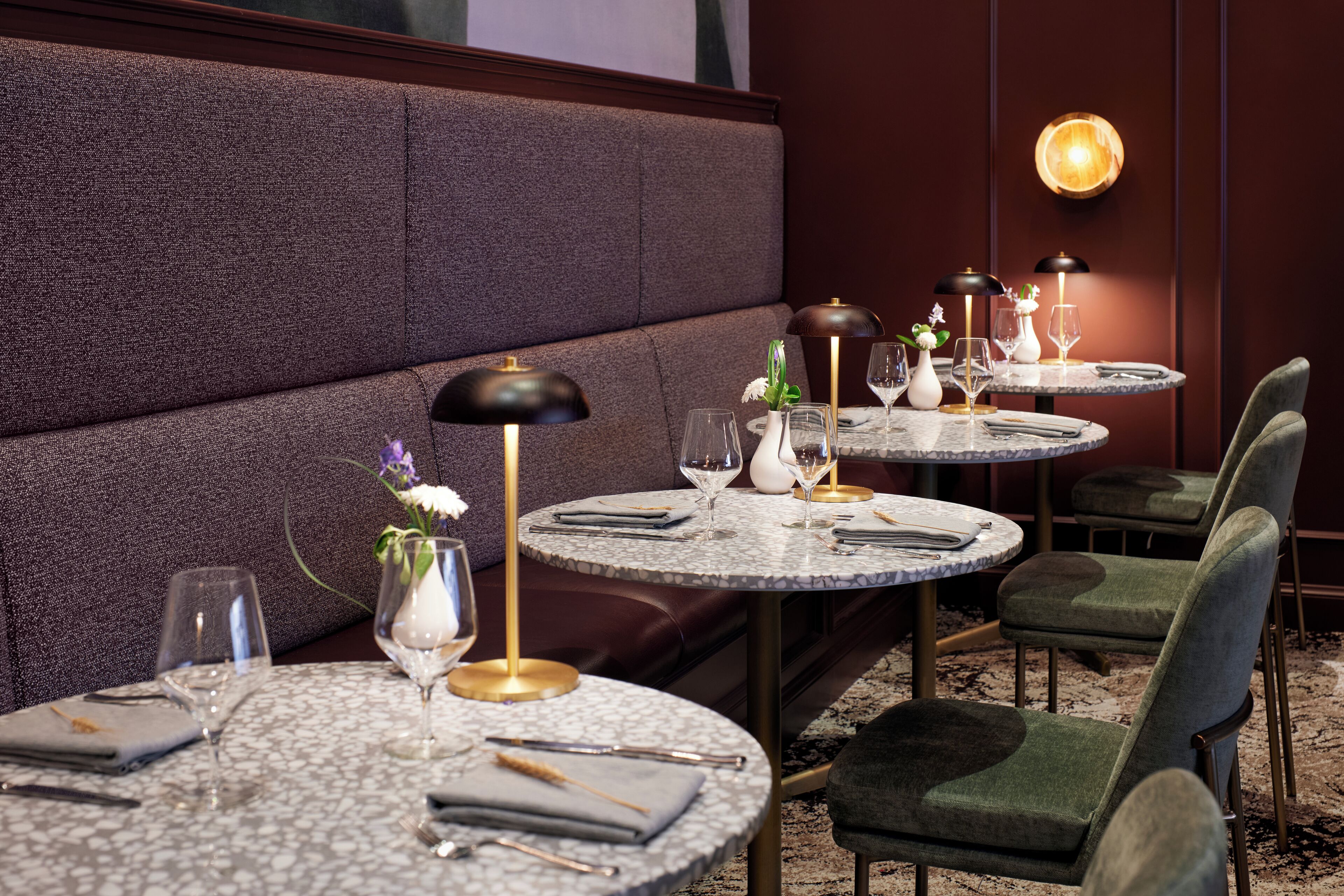 A restaurant with round tables, green upholstered chairs, and a marble floor.