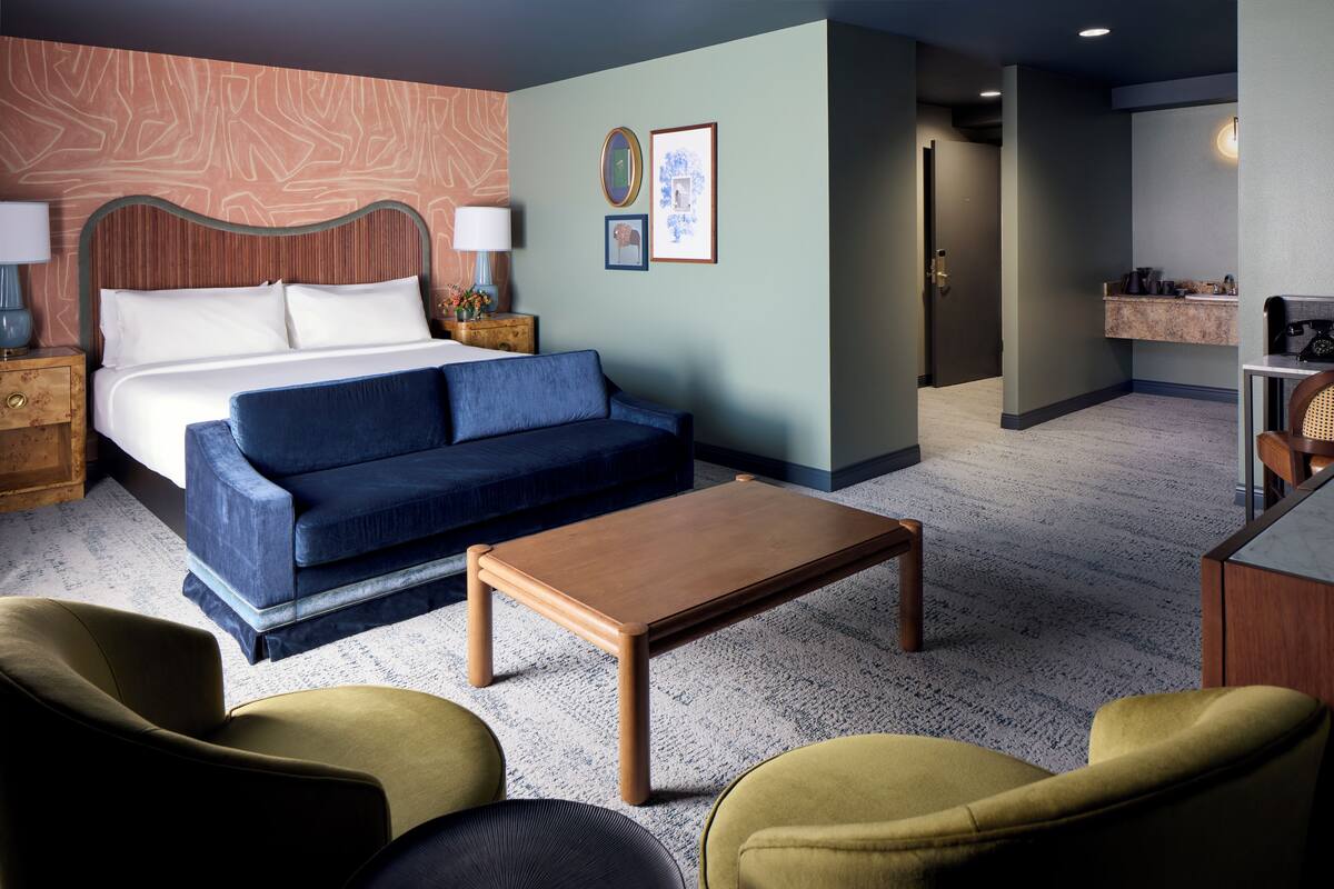 A hotel room with a bed, a sofa, a coffee table, and a desk area.