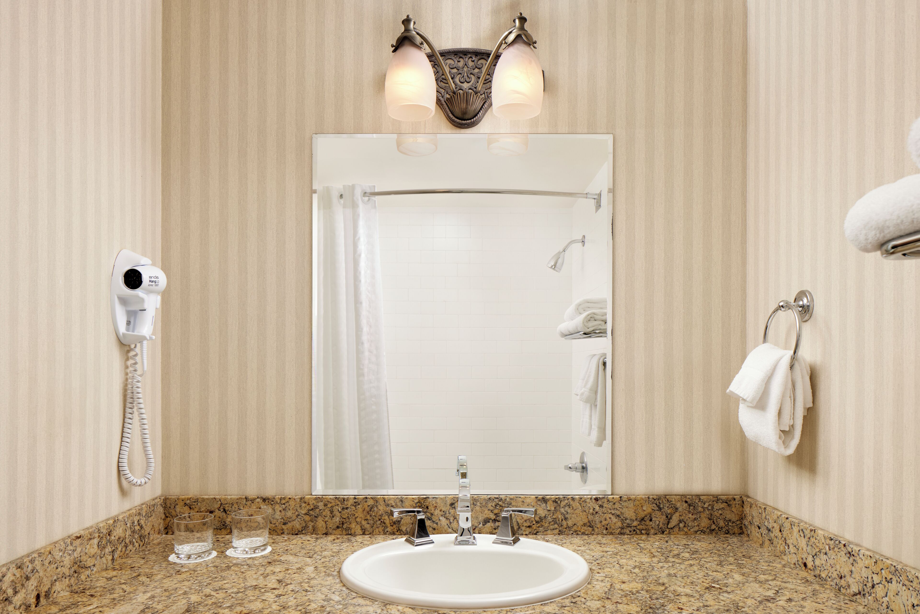 Un baño con encimera de granito, lavamanos blanco, espejo, toallero y secador de pelo.