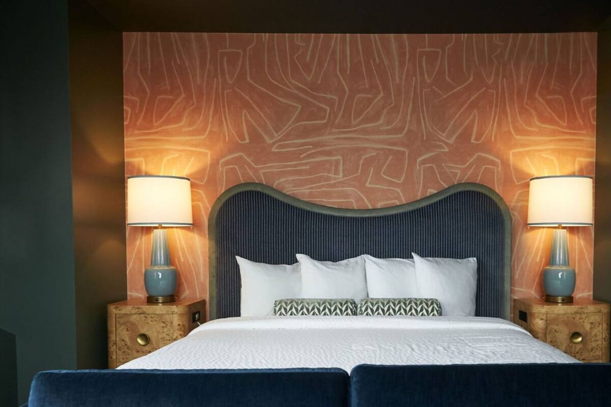 A bed with a dark headboard, two bedside lamps, and a patterned wall behind.