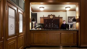 A reception desk with a wooden finish, two lamps, a safe deposit box, and a clock on the wall. - The Marcus Whitman Hotel (Walla Walla)