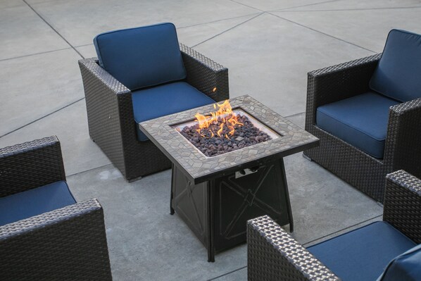A patio with wicker furniture and a square fire pit. - Lions Gate Hotel (McClellan)