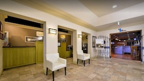 A spacious lobby with a kitchen area, two white armchairs, and a bar area with a counter.