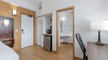 A hotel room with a bed, a desk with a lamp, a refrigerator, and a microwave.