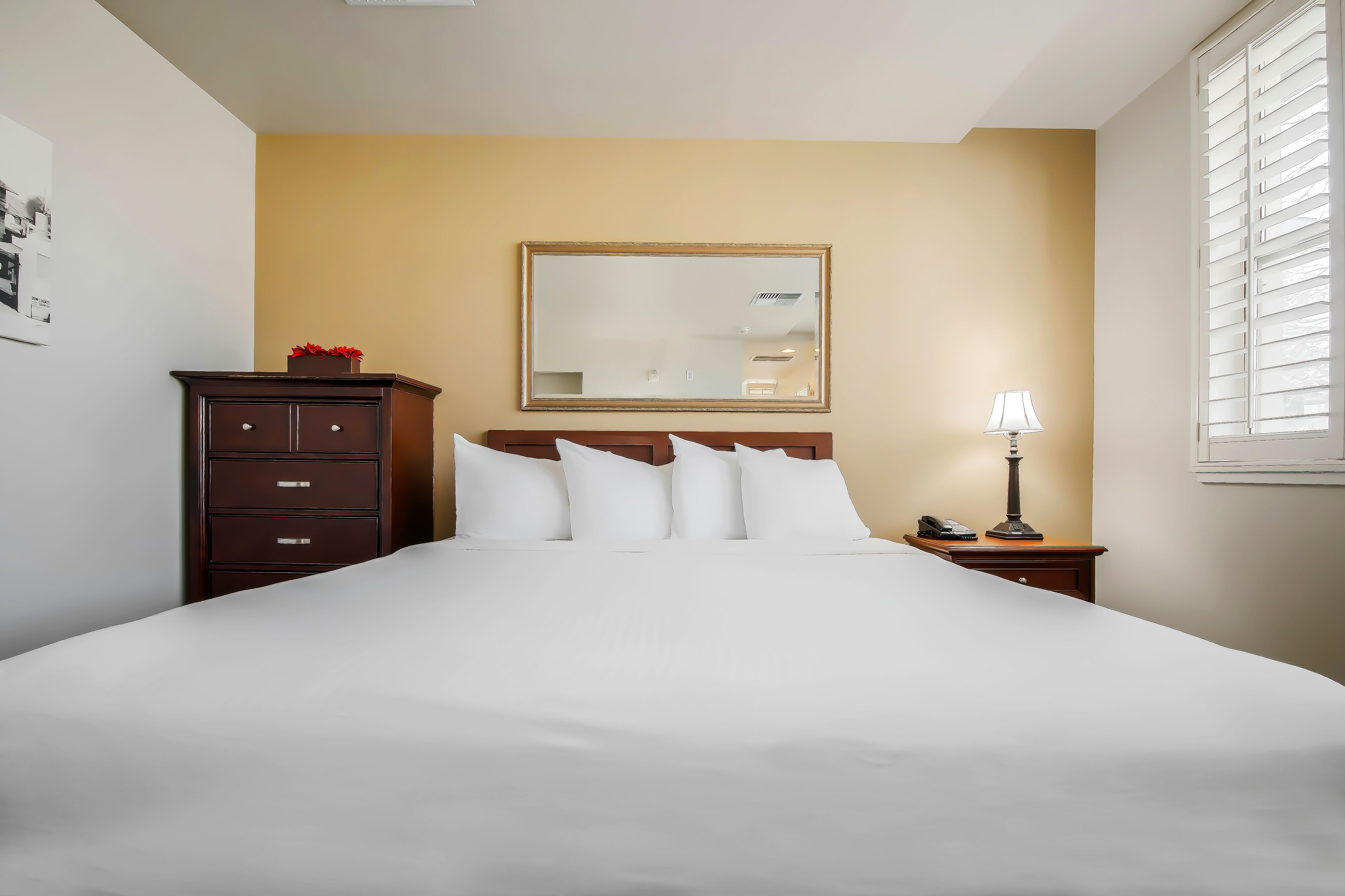 Habitación de hotel con una cama grande, un aparador, una mesita de noche con lámpara y un espejo en la pared.