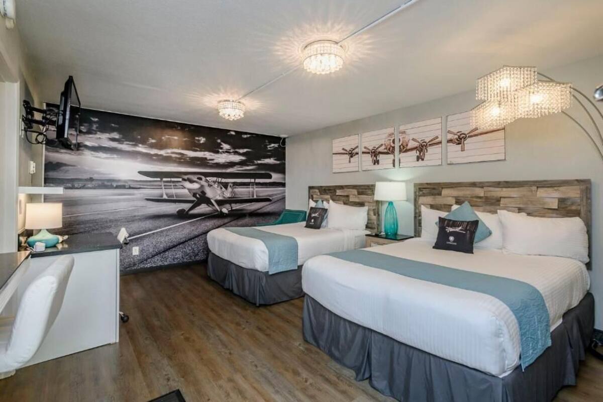 A hotel room with two beds, a desk, a chair, a large wall mural, and a chandelier.