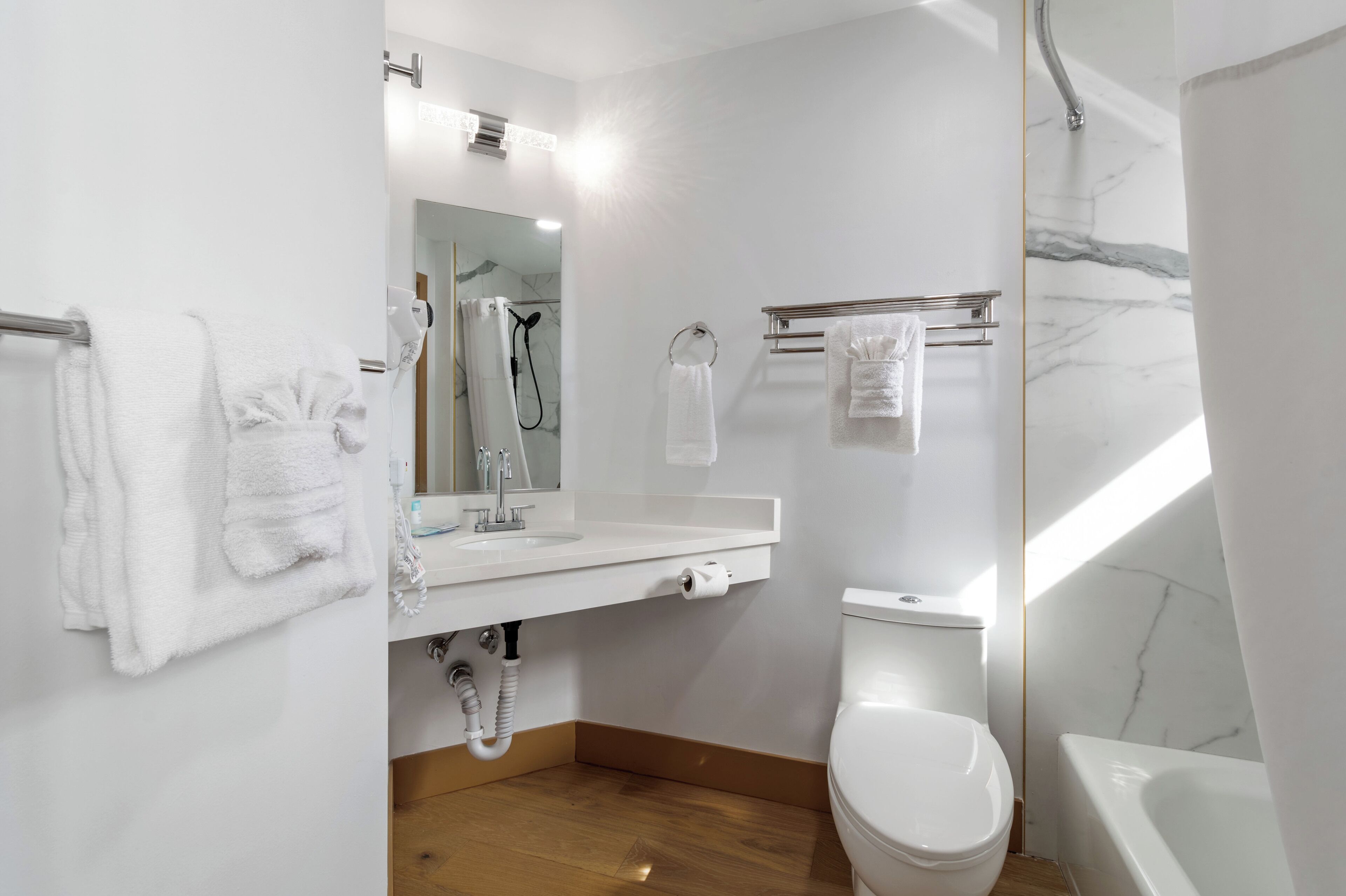 Un baño moderno con lavamanos, espejo, inodoro y ducha blancos.