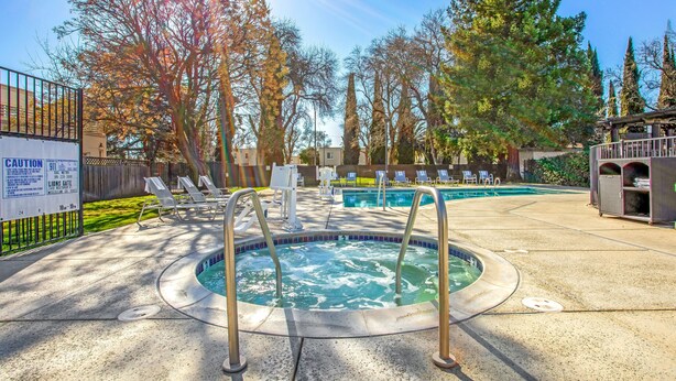 A pool area with a hot tub, lounge chairs, and a caution sign.