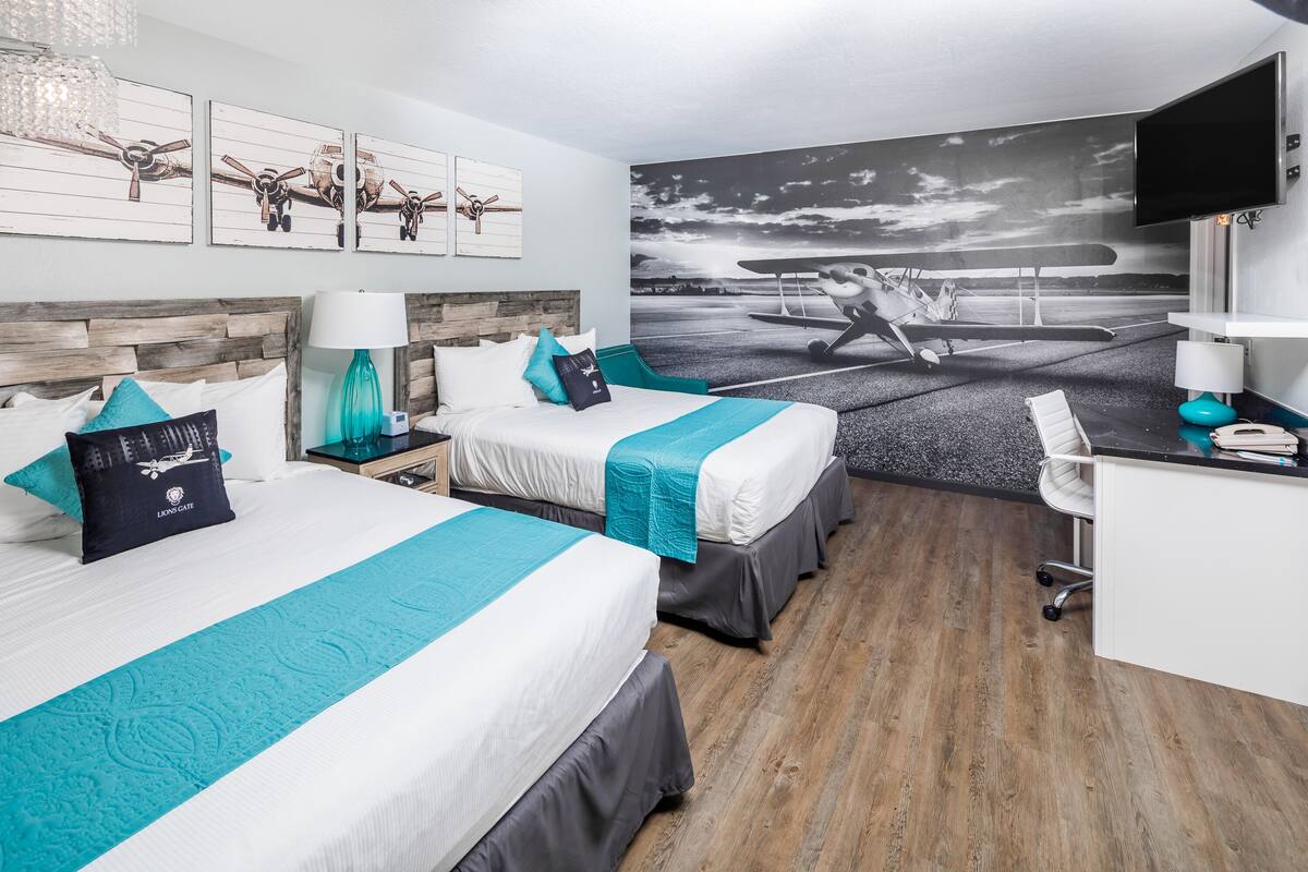 A hotel room with two beds, a desk, and a large airplane mural on the wall.