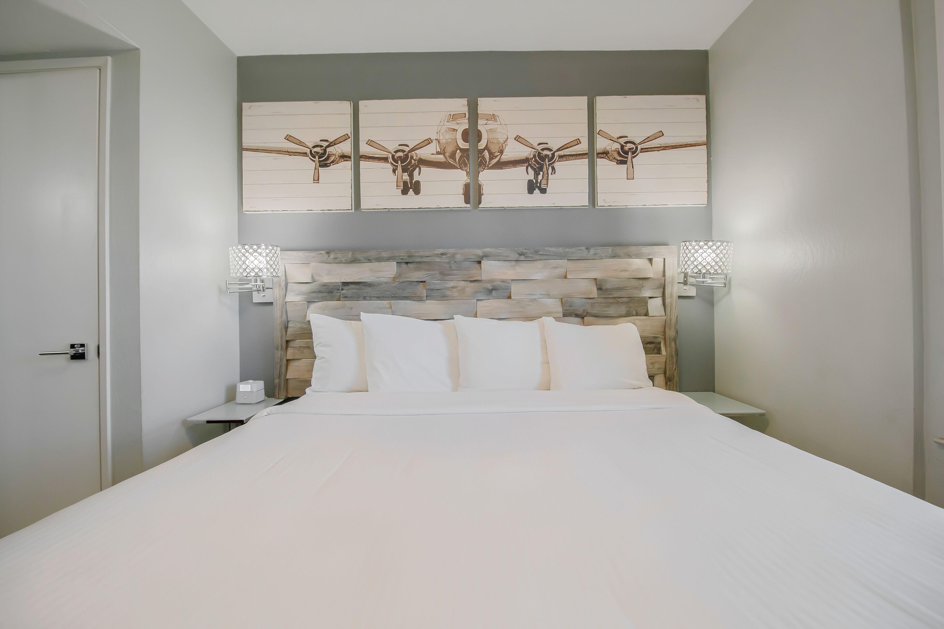 Une chambre avec un grand lit, une tête de lit en pierre et une œuvre d’art représentant un avion accrochée au mur.