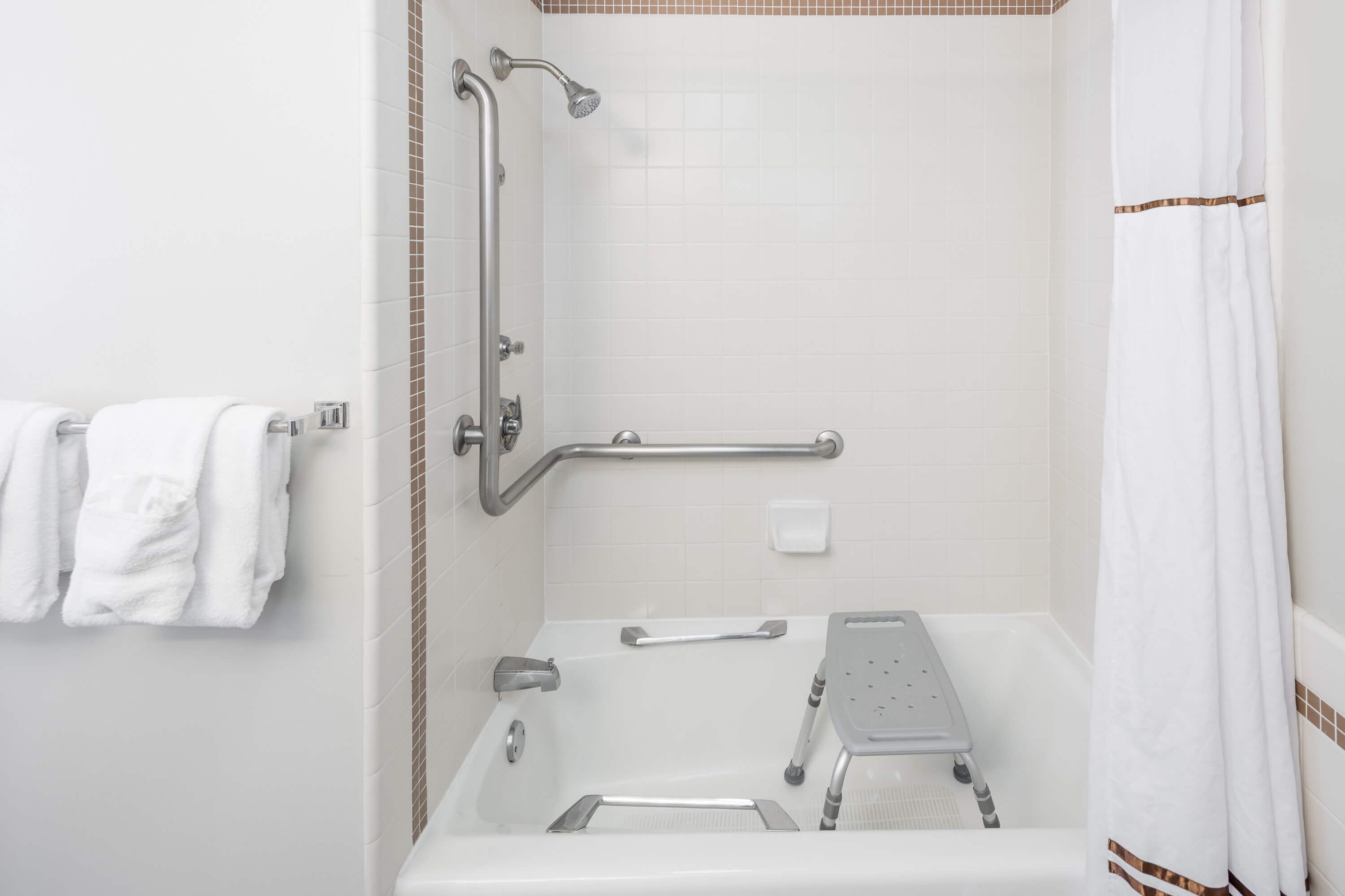 Een badkamer met een inloopdouche, handgrepen, een opstapje en een handdoekhouder.