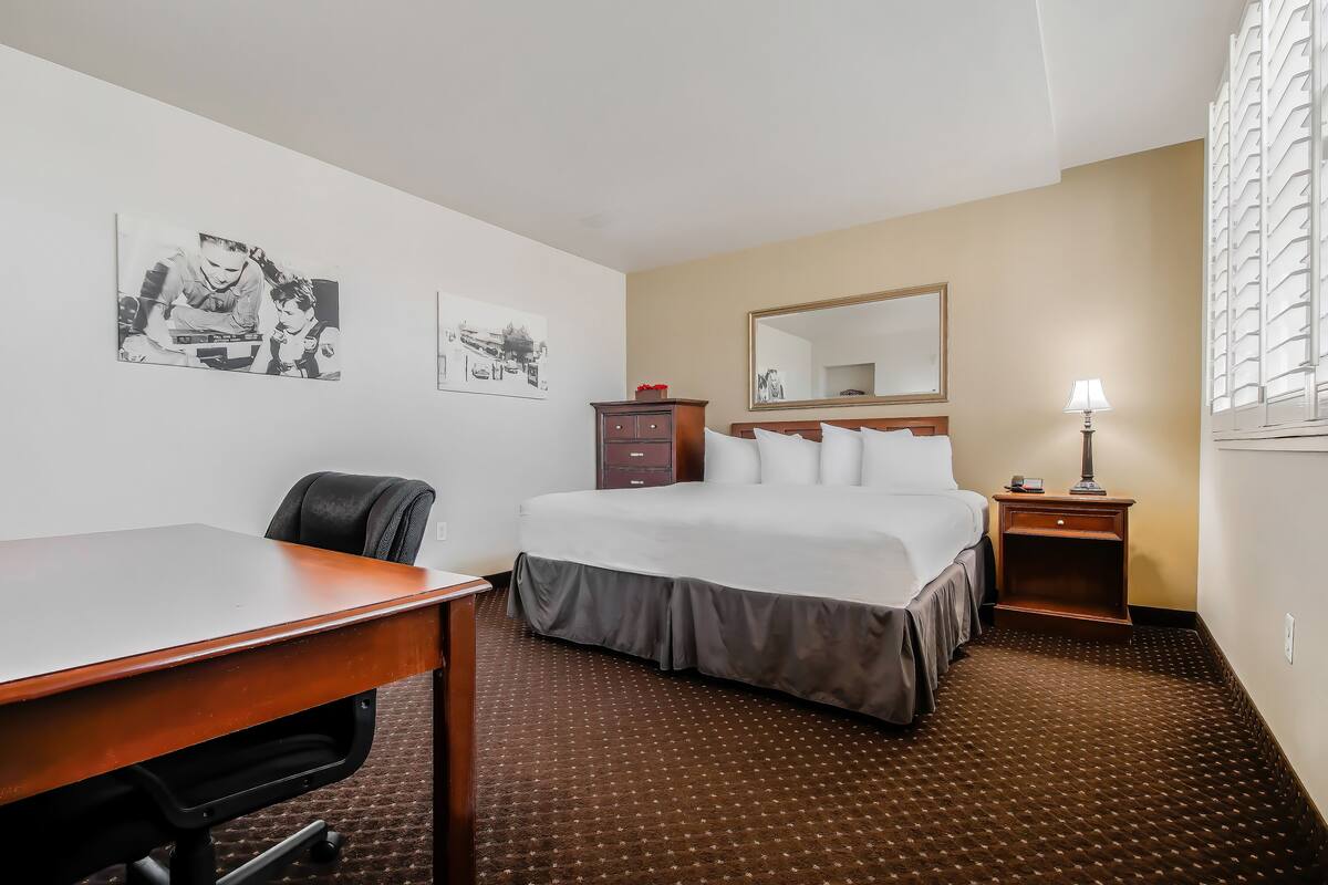 A hotel room with a bed, a desk, a chair, a dresser, a mirror, and a lamp.
