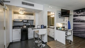 A compact kitchen with white cabinets, a microwave, a sink, and a bar area with stools.