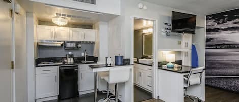 A compact kitchen with white cabinets, a microwave, a sink, and a bar area with stools.