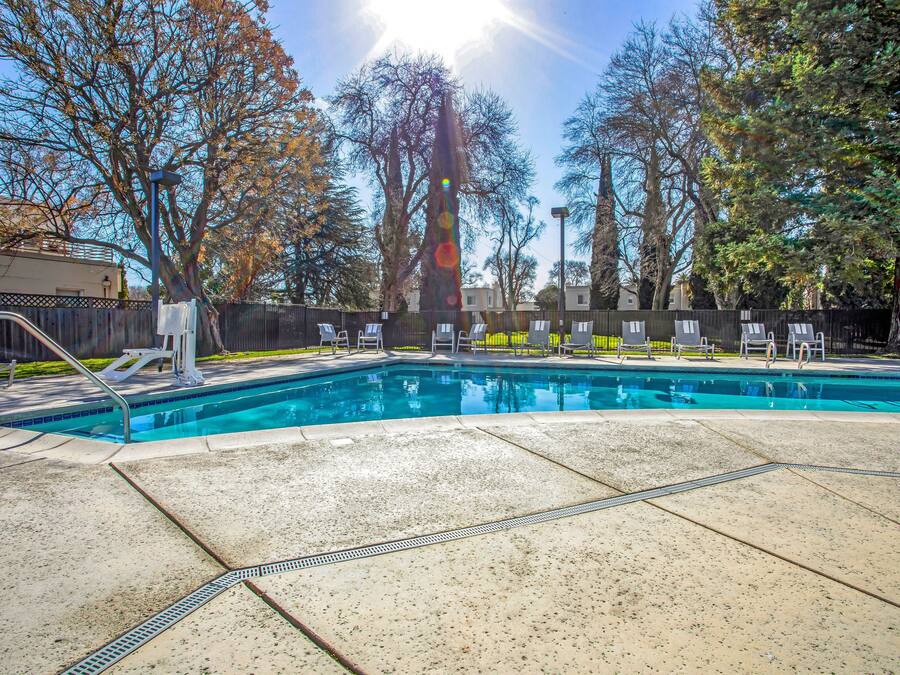 Una piscina con solárium de baldosas, rodeada de árboles y una valla.