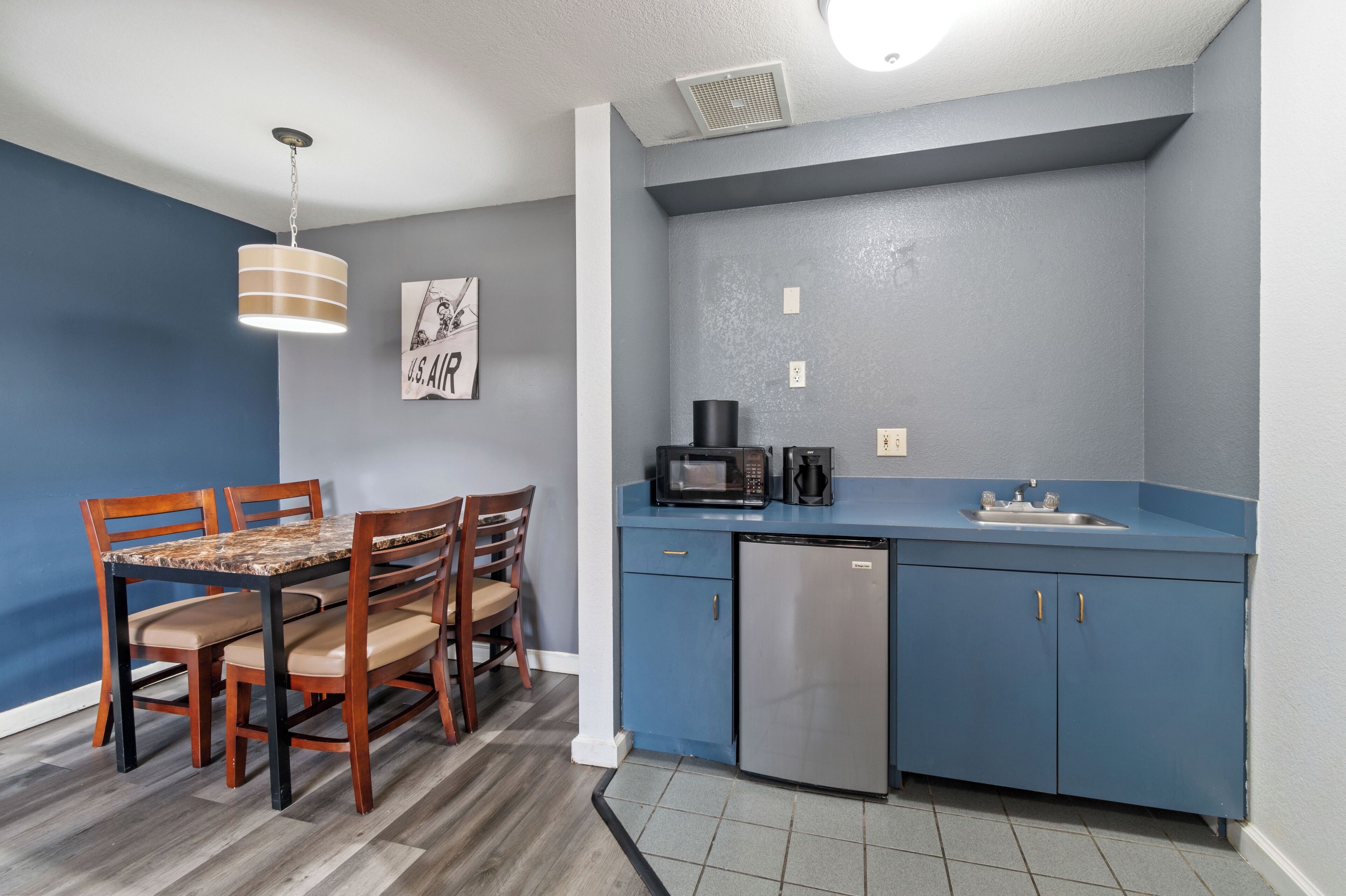 A compact kitchen with a blue countertop, a microwave, a coffee maker, and a refrigerator.