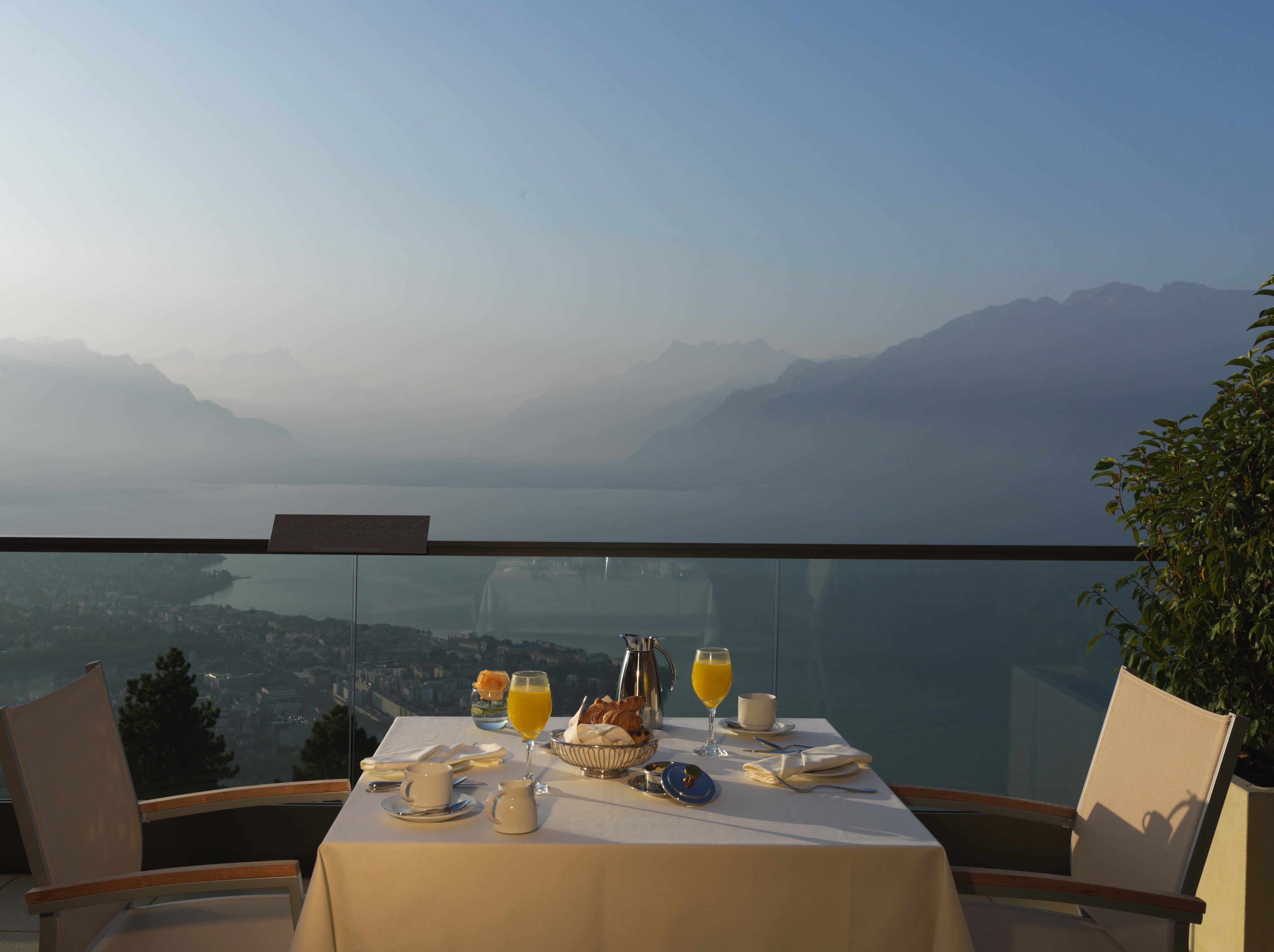 A table set for breakfast with a view of mountains and a lake.