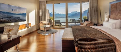 A hotel room with a large bed, a desk, a chair, a sofa, a TV, and a balcony with a mountain view.