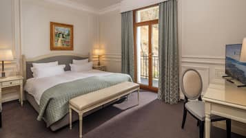 A hotel room with a bed, bedside tables, a desk, a chair, a window with curtains, and a painting on the wall.