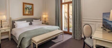 A hotel room with a bed, bedside tables, a desk, a chair, a window with curtains, and a painting on the wall.