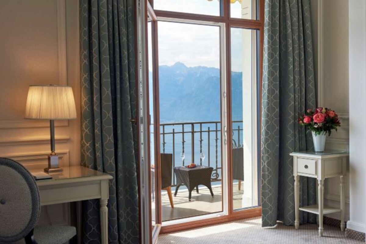 A hotel room with a large sliding glass door leading to a balcony with a mountain view.