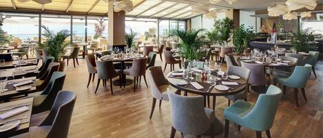 A spacious restaurant with multiple dining areas, large windows, and modern pendant lighting.