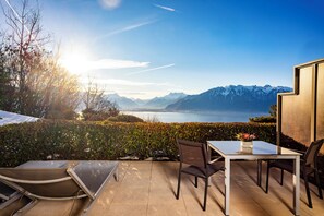 Une terrasse avec une table et des chaises, une vue sur les montagnes et un plan d’eau.