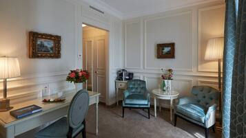 Habitación de hotel con escritorio, dos sillas, una mesita con lámpara y dos cuadros en las paredes.