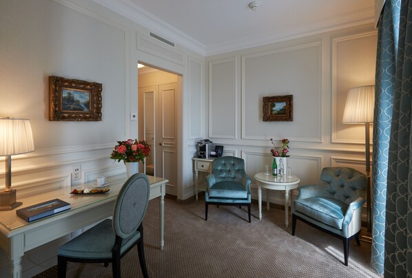Habitación de hotel con escritorio, dos sillas, una mesita con lámpara y dos cuadros en las paredes.