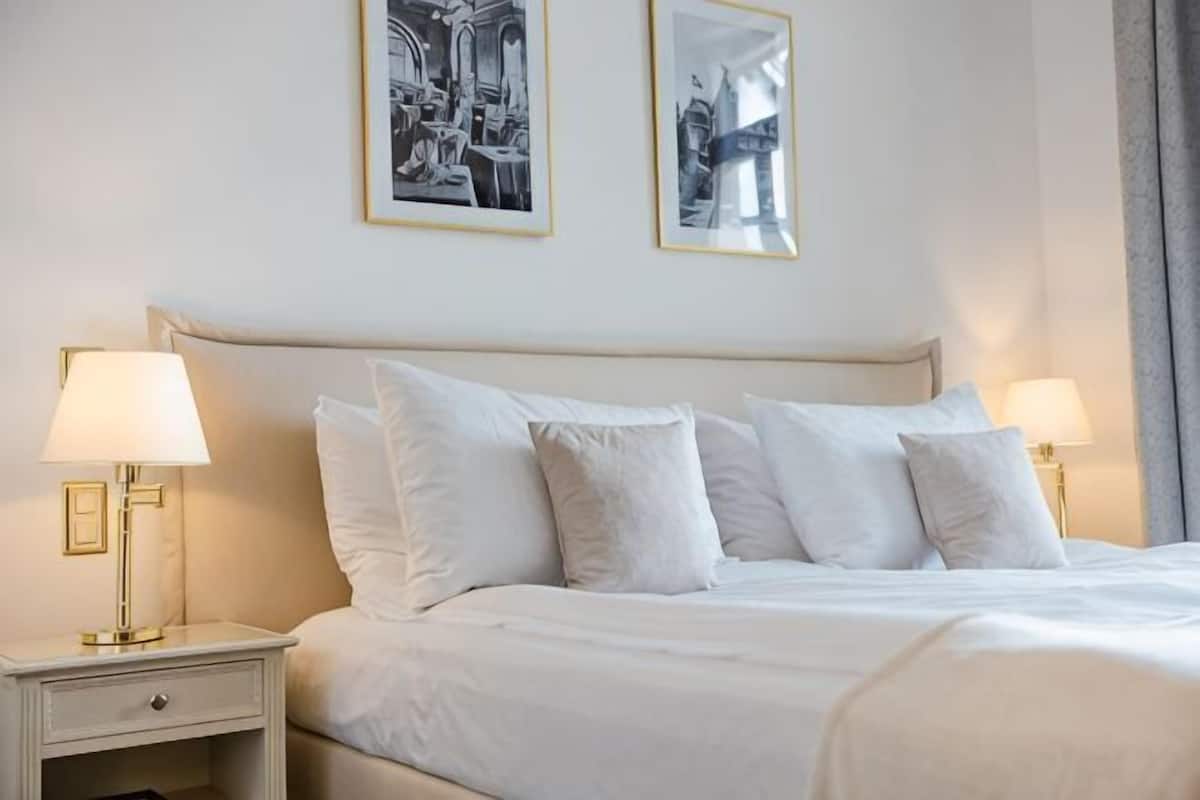 Ein ordentlich bezogenes Bett mit weißen Leinentüchern, zwei Nachttischlampen und zwei gerahmte Bilder an der Wand.